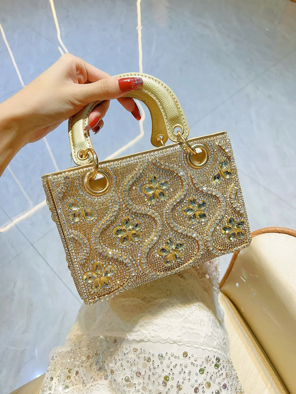 Pochette soirée femme en satin noir avec chaîne en métal, ornée de strass et diamants pour un look élégant et luxueux.
